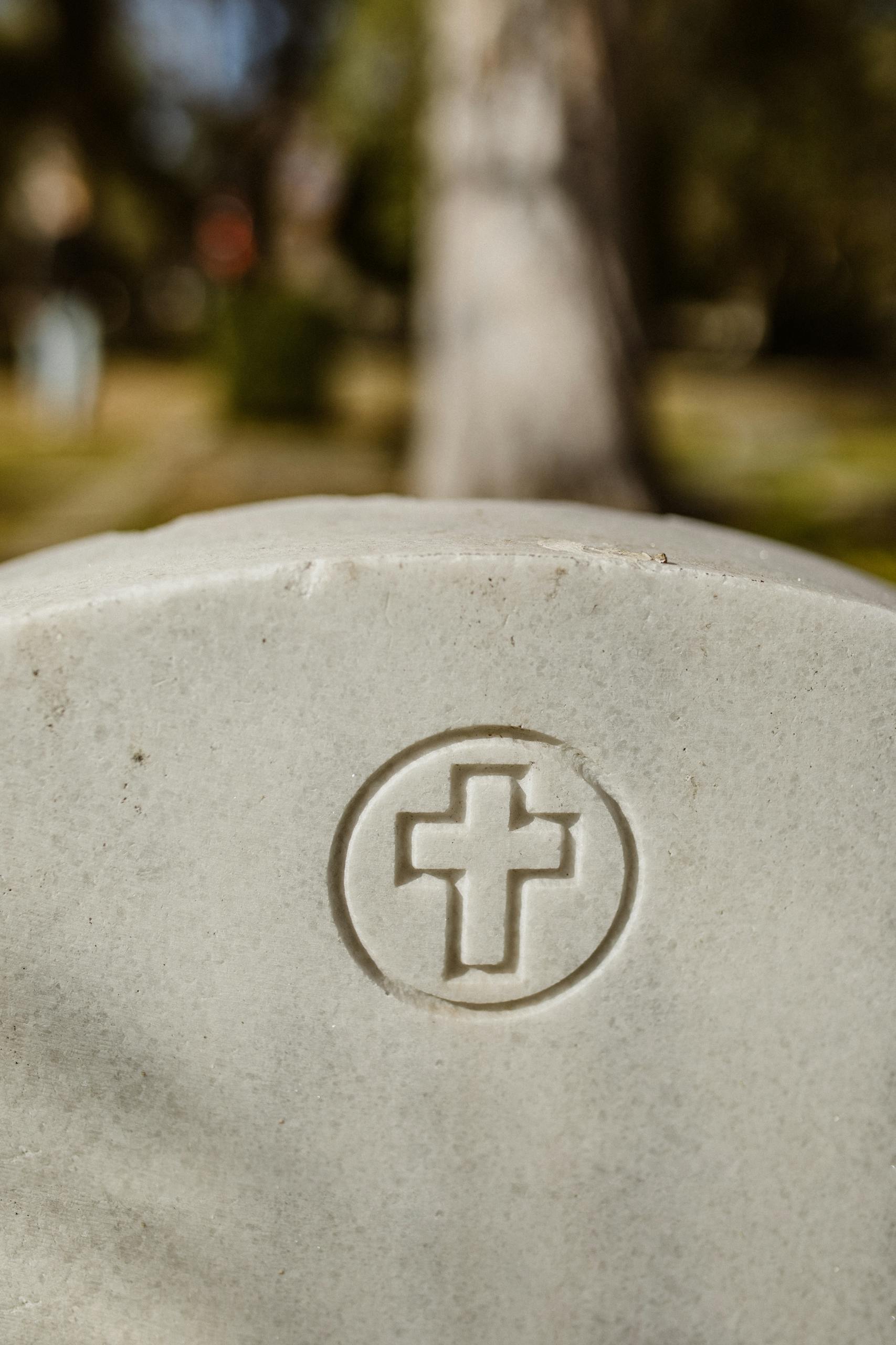 A detailed view of a gravestone featuring a cross engraving in an outdoor cemetery setting.