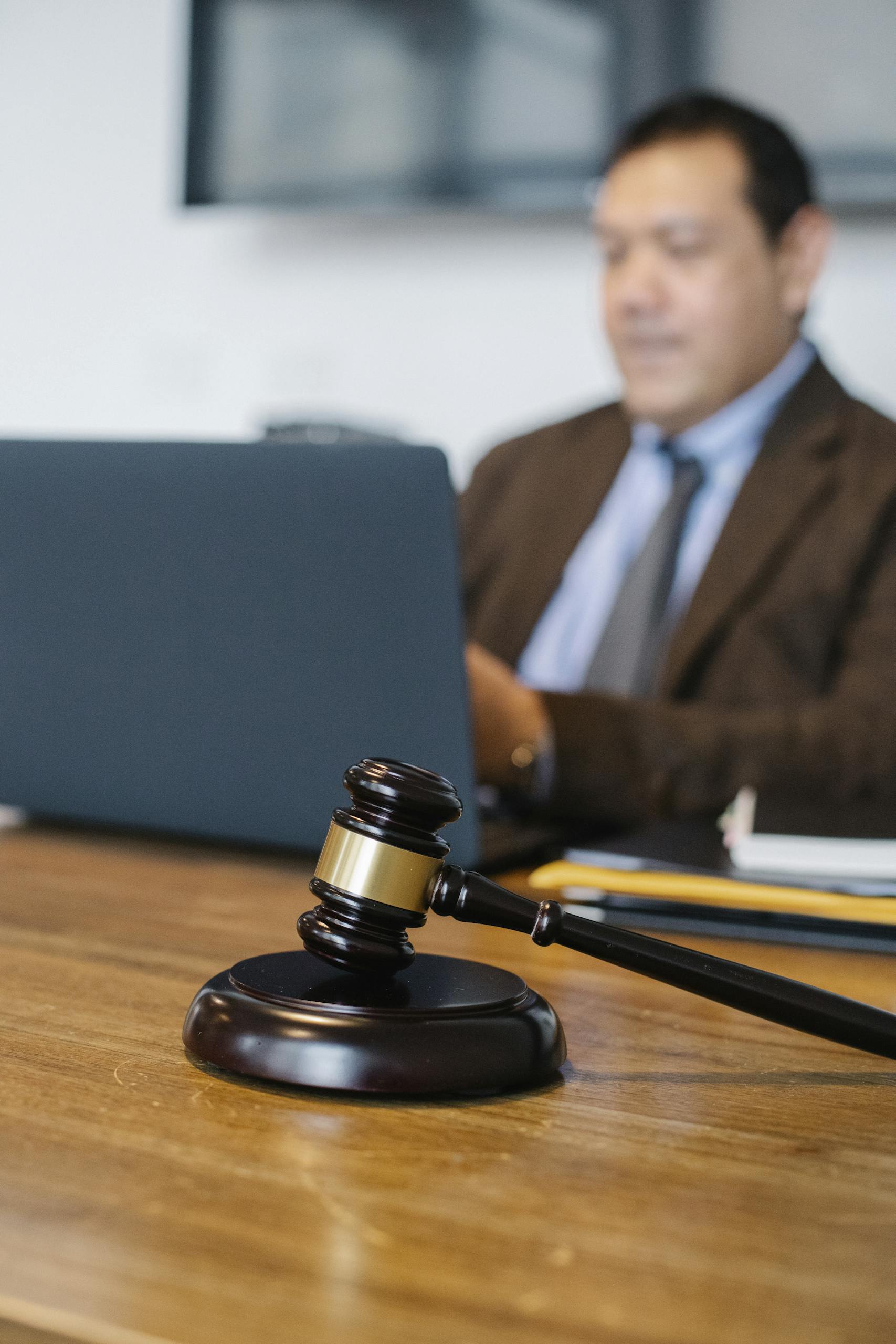 A focused lawyer working on a laptop with a gavel on the desk, indicating legal proceedings.